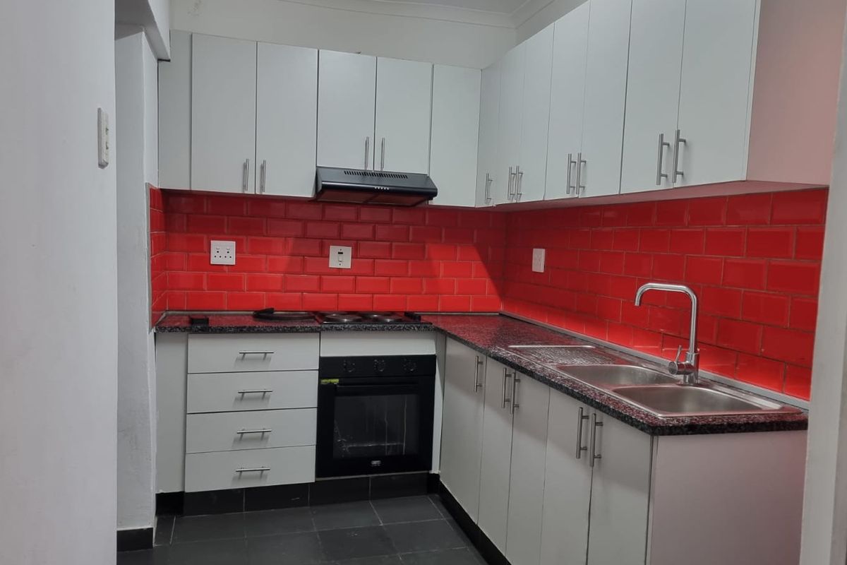 A compact, modern kitchen featuring white cabinetry, granite countertops, a striking red subway tile backsplash, and integrated appliances including an oven and hob.