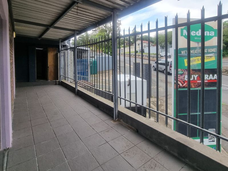 A covered outdoor patio area featuring tiled flooring and metal security fencing, overlooking a street-side commercial signage board.