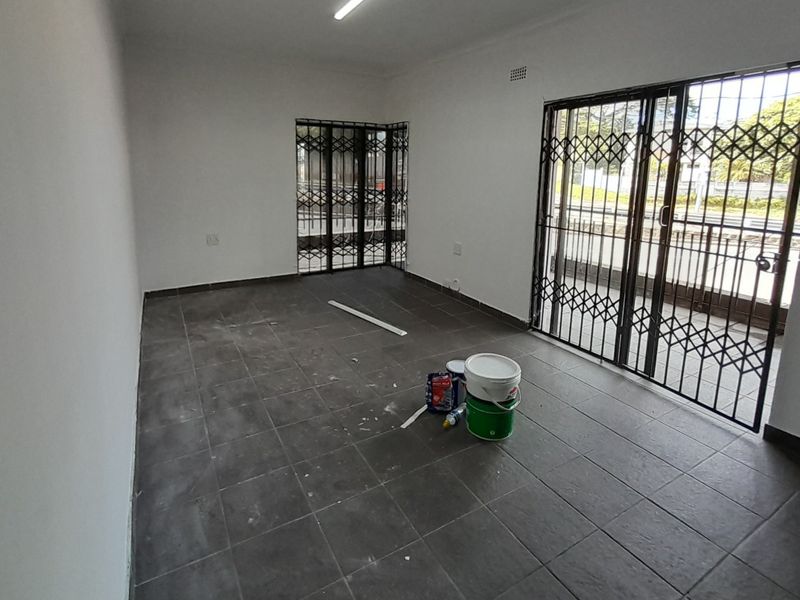 An empty living area featuring dark tiled flooring, security gates, and sliding glass doors leading to an outdoor space.