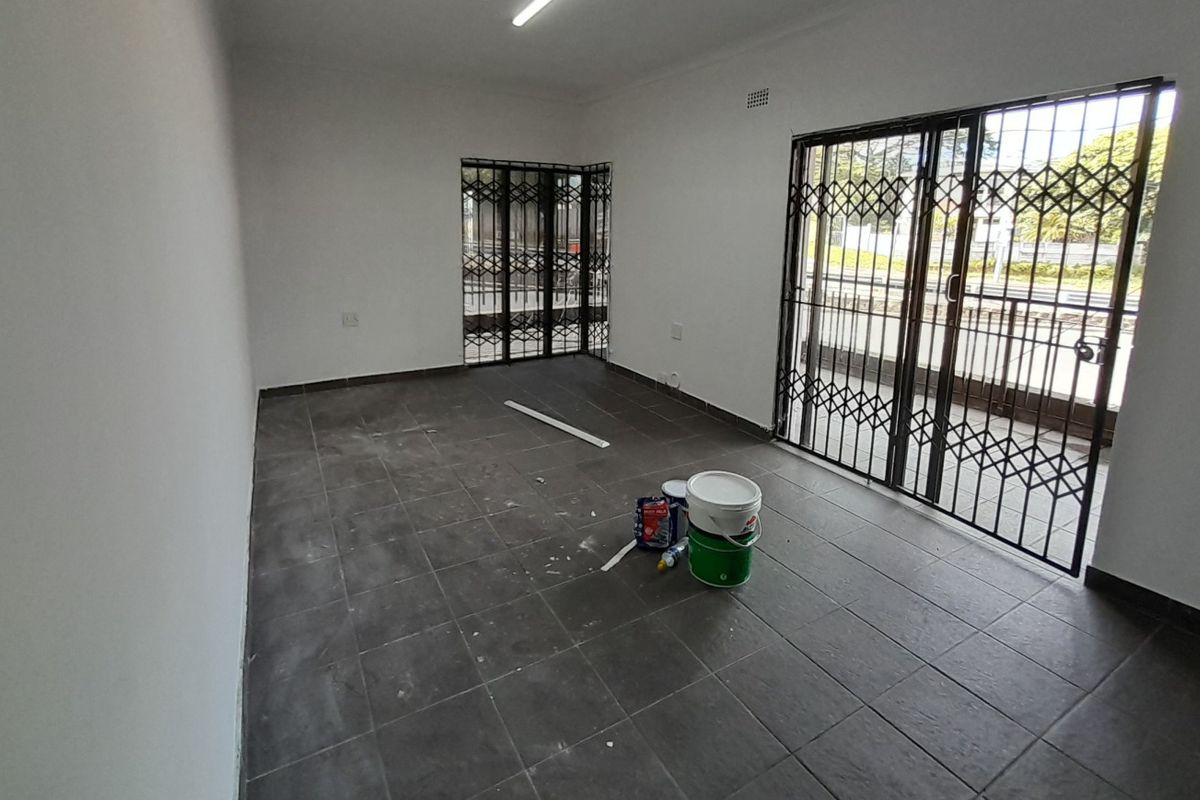 An empty living area featuring dark tiled flooring, security gates, and sliding glass doors leading to an outdoor space.