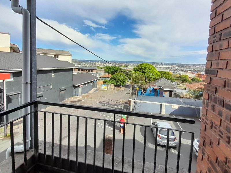 A balcony view overlooking the street and surrounding neighbourhood, featuring a metal balustrade and exposed brick wall.