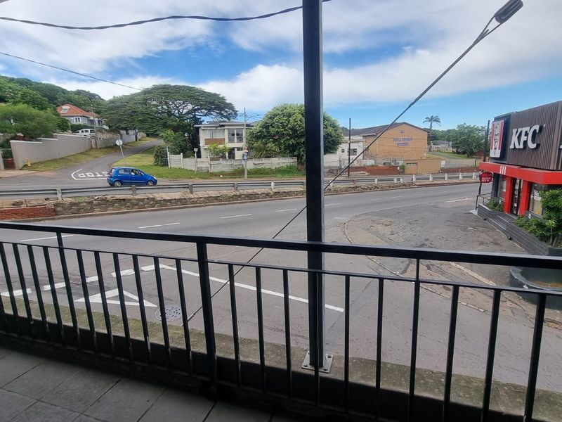 A covered balcony area featuring tiled flooring and a metal balustrade, offering an elevated view of the surrounding street and commercial area.