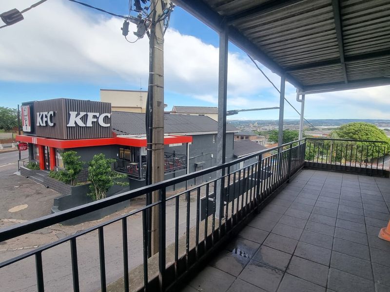 A covered balcony featuring tiled flooring and metal railings, offering an elevated view of the surrounding neighborhood and commercial area.