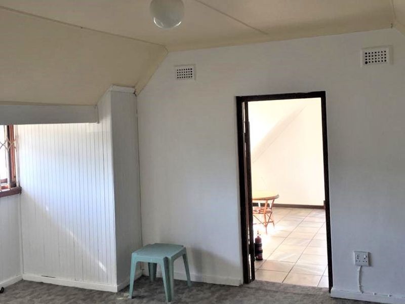 An empty bedroom featuring a sloped ceiling, security bars on the window, and ventilation grilles, presenting a blank canvas for renovation.