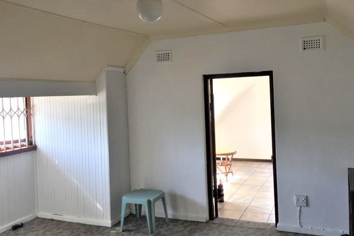 An empty bedroom featuring a sloped ceiling, security bars on the window, and ventilation grilles, presenting a blank canvas for renovation.