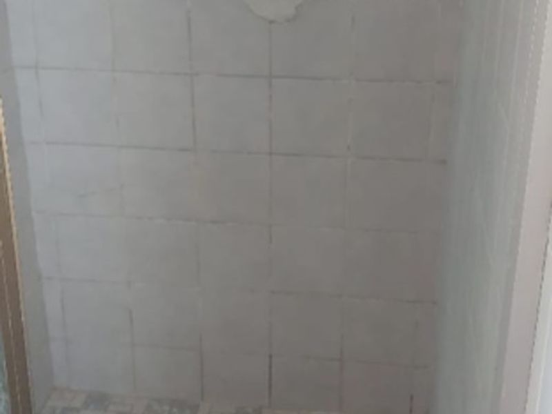 A dated shower enclosure requiring maintenance, featuring worn floor tiles and damaged wall finishes around the shower mixer.