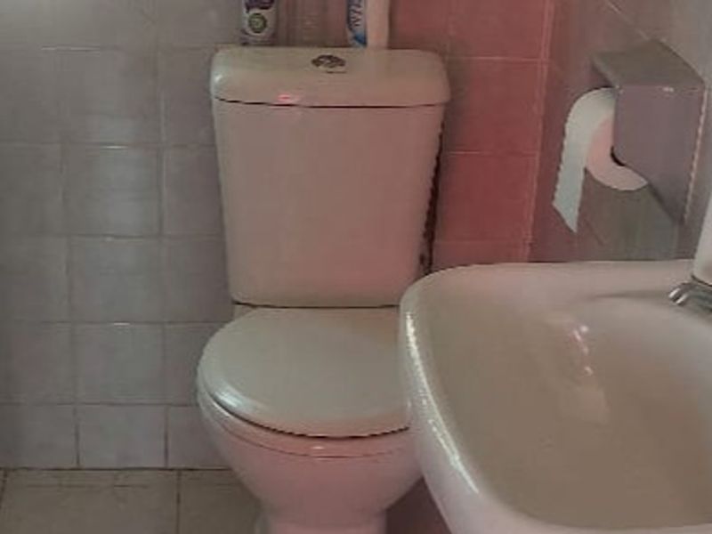 A compact bathroom featuring a standard ceramic toilet and washbasin with wall and floor tiling, requiring cosmetic updates to improve the overall finish.