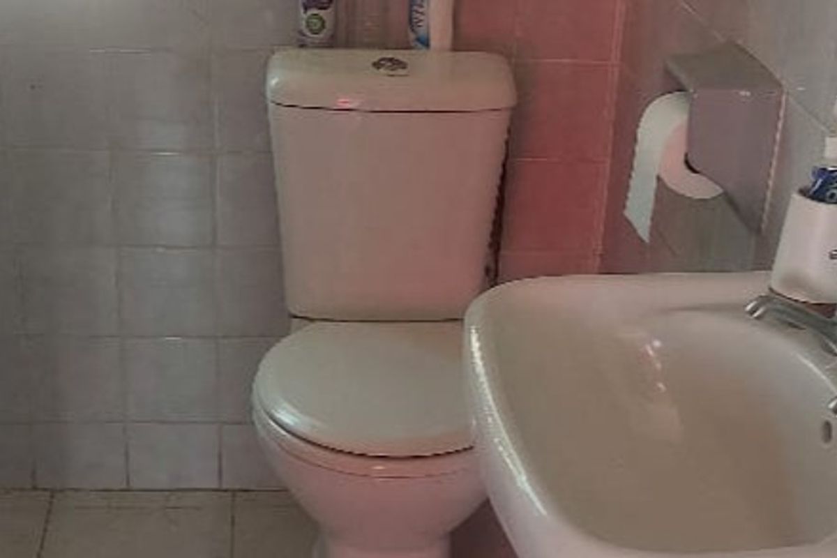 A compact bathroom featuring a standard ceramic toilet and washbasin with wall and floor tiling, requiring cosmetic updates to improve the overall finish.