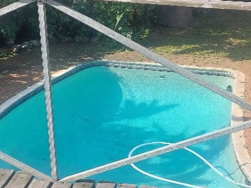 Outdoor swimming pool area featuring brick paving and a metal safety fence, viewed from an elevated position.