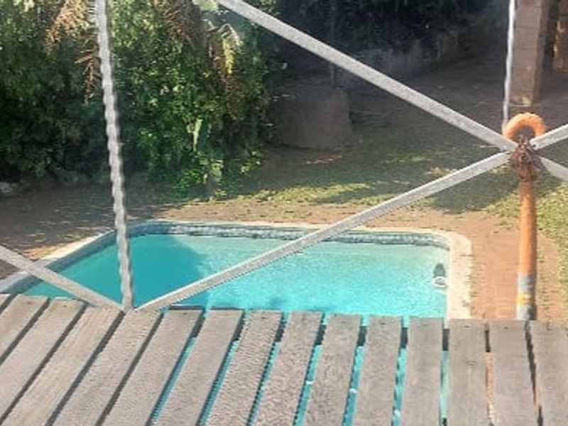 An elevated view of a swimming pool and garden area, featuring wooden decking and a metal safety railing.