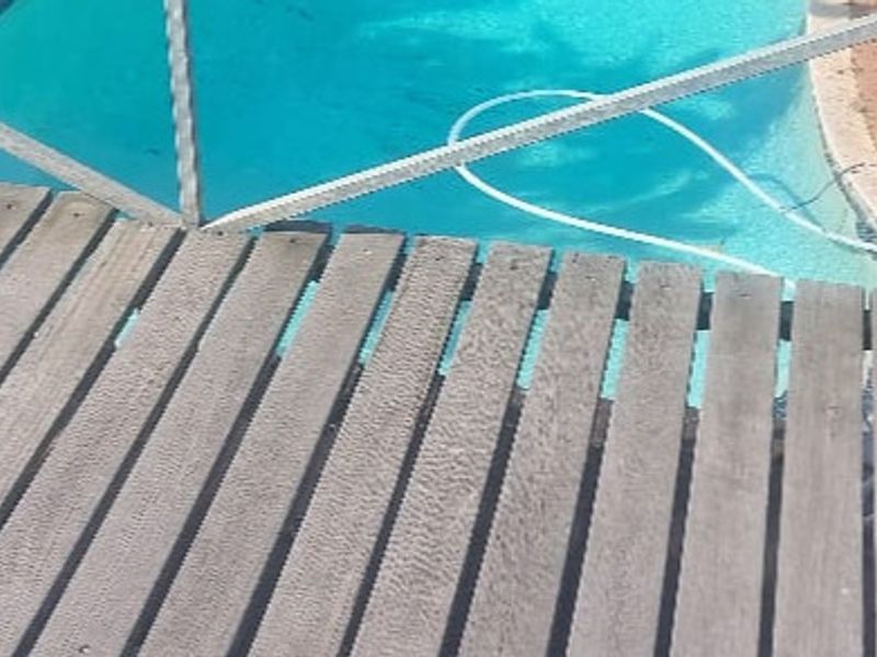 An outdoor swimming pool area featuring a wooden deck and a safety fence, showing signs of wear and weathering.