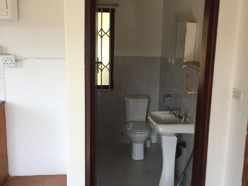 A compact bathroom featuring a pedestal washbasin and toilet, with tiled walls and flooring, requiring cosmetic updates to modernize the space.