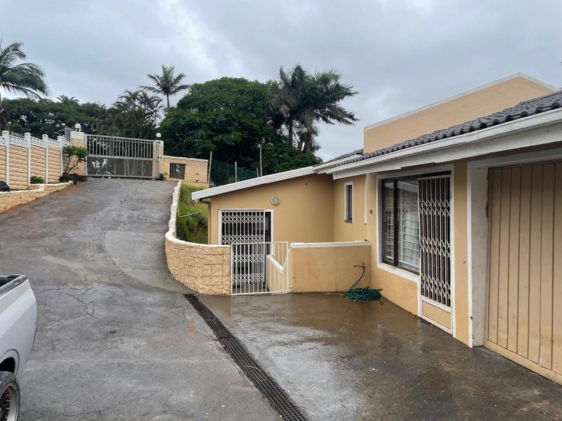 Exterior view of the property featuring a concrete driveway, retaining wall, and secure gated entrance with tiled roof and security bars on windows.