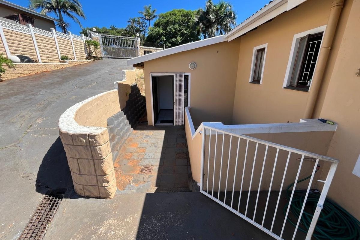 Rear exterior area featuring a paved walkway, retaining wall, and metal security gate access to the property.