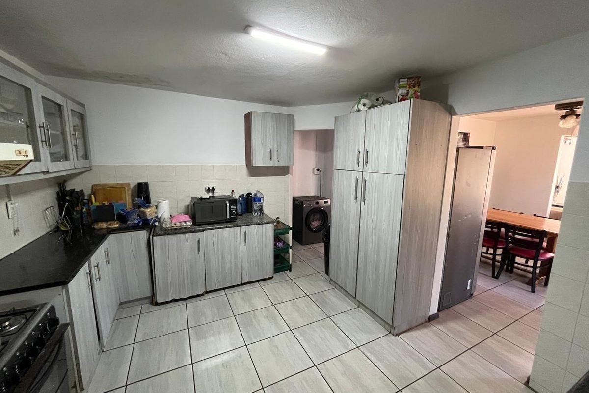 Functional kitchen featuring light wood-grain cabinetry, dark countertops, tiled flooring, and a dedicated laundry nook, with an adjacent dining area visible.