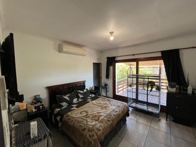 A bedroom featuring tiled flooring, a wall-mounted air conditioning unit, and sliding glass doors providing access to an outdoor deck area.