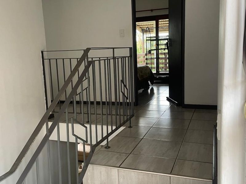 A tiled hallway landing featuring a metal staircase railing and access to an adjacent bedroom.