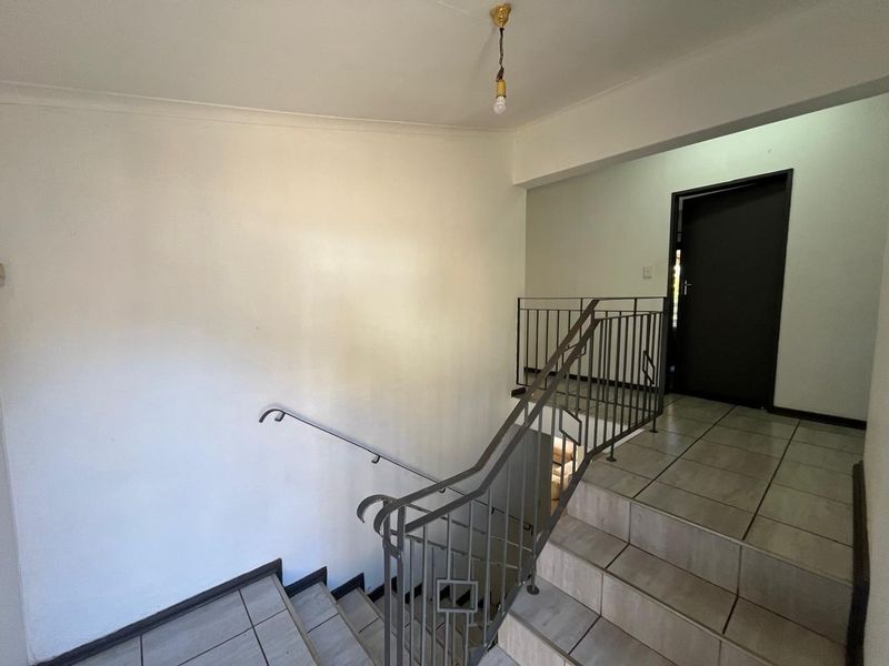 A functional hallway and staircase area featuring tiled steps, metal balustrades, and a neutral color palette, providing access to upper levels.
