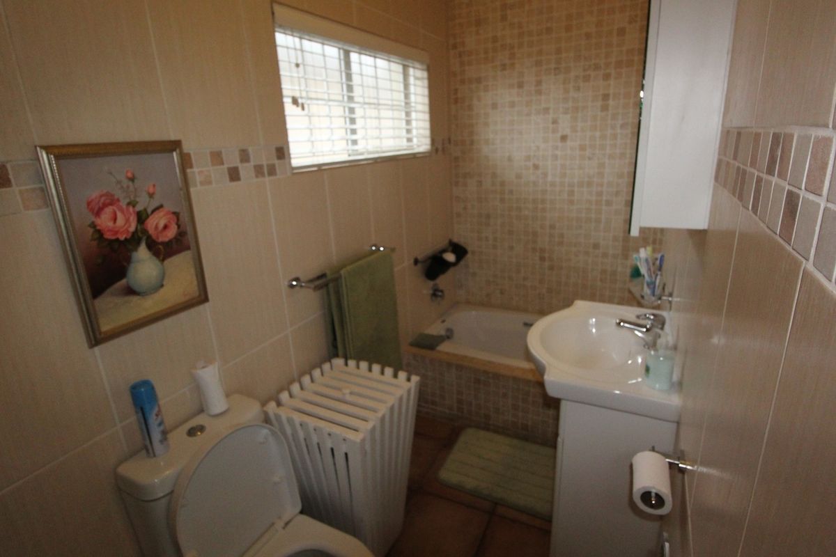 A compact bathroom featuring a pedestal washbasin, built-in bathtub, and toilet, finished with neutral wall and floor tiling.