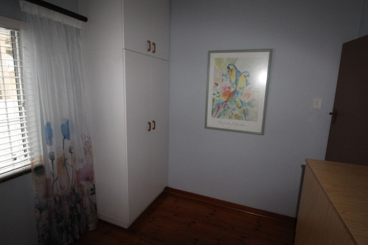 A bedroom featuring built-in cupboards, wooden flooring, and a window with venetian blinds.