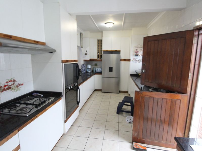 A functional kitchen featuring white cabinetry, granite countertops, a gas hob, built-in oven, and tiled flooring, with a traditional wooden stable door.