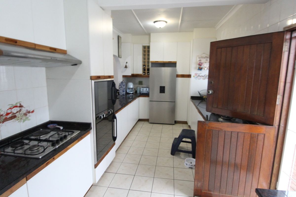 A functional kitchen featuring white cabinetry, granite countertops, a gas hob, built-in oven, and tiled flooring, with a traditional wooden stable door.