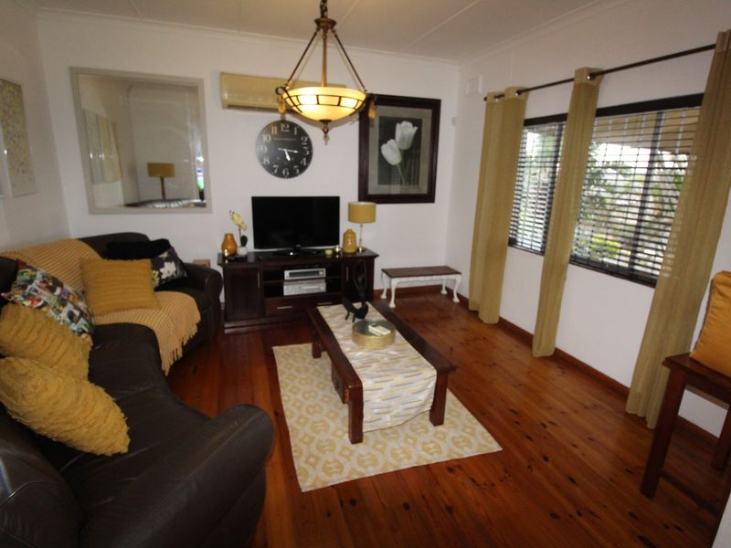 A comfortable living room featuring polished timber flooring, a wall-mounted split system air conditioner, and large windows with venetian blinds.
