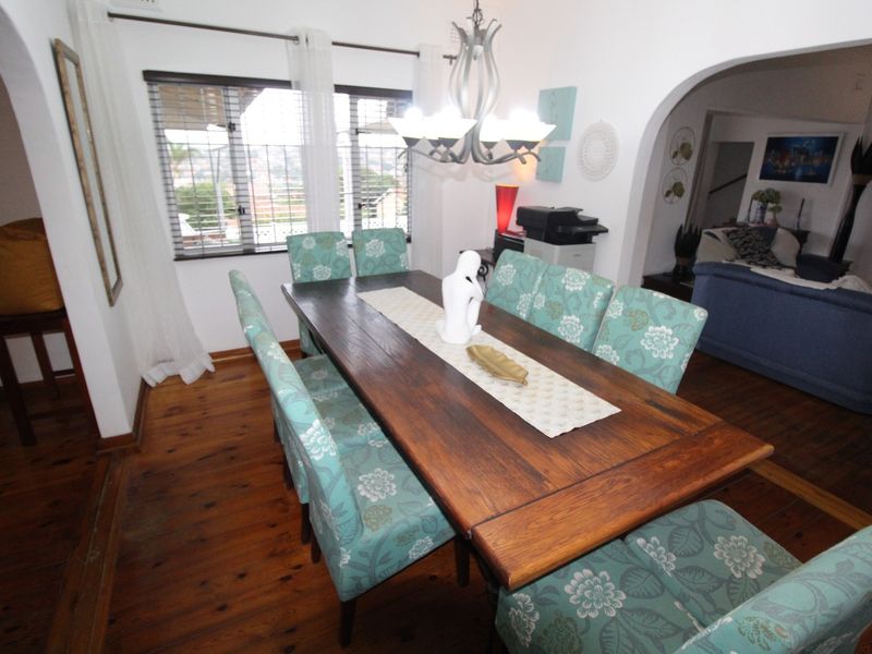 A dining room featuring polished hardwood flooring, a decorative chandelier, and an arched entryway leading to the adjacent living area.