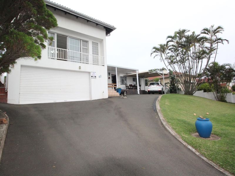 Front view of a two-story house featuring an asphalt driveway, double garage, upper-level balcony, and a covered patio area.