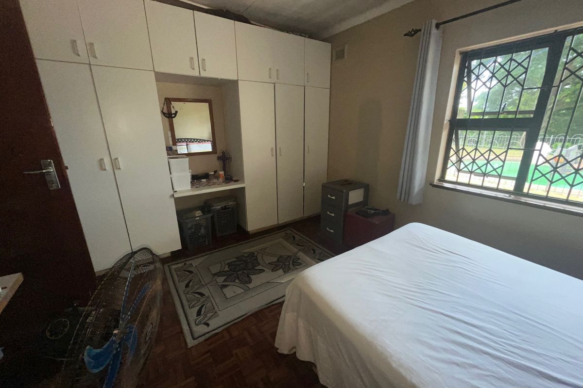 A bedroom featuring built-in white cabinetry, parquet flooring, and a window with security bars overlooking the pool area.