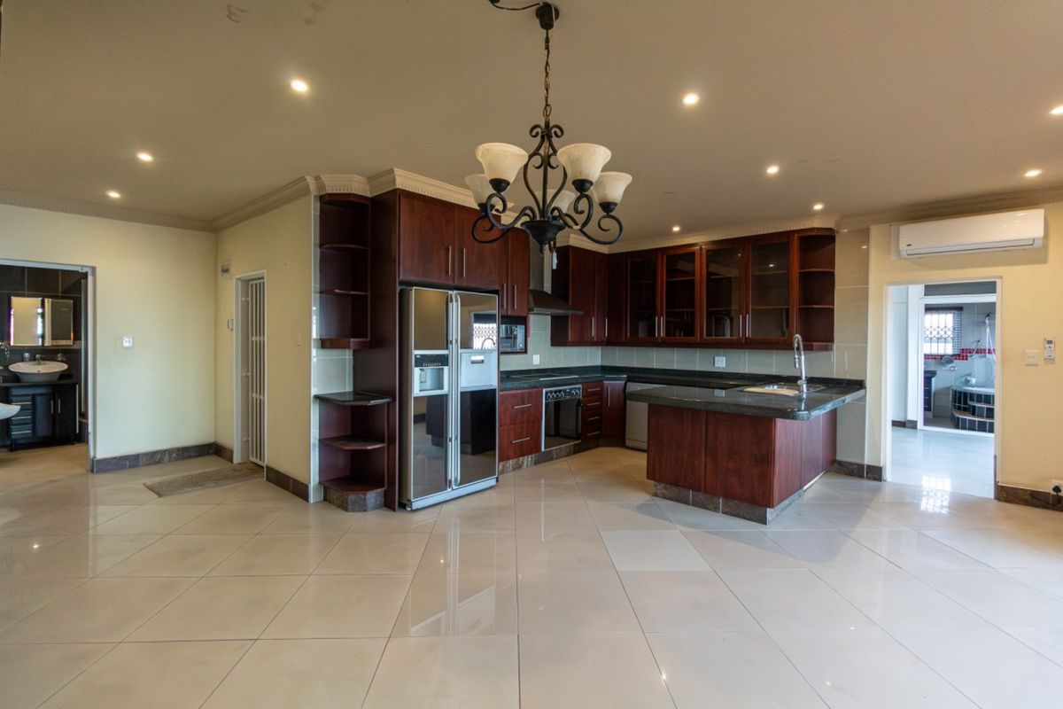Spacious kitchen featuring dark wood cabinetry, granite countertops, integrated appliances, and tiled flooring, with an open-plan layout and recessed lighting.