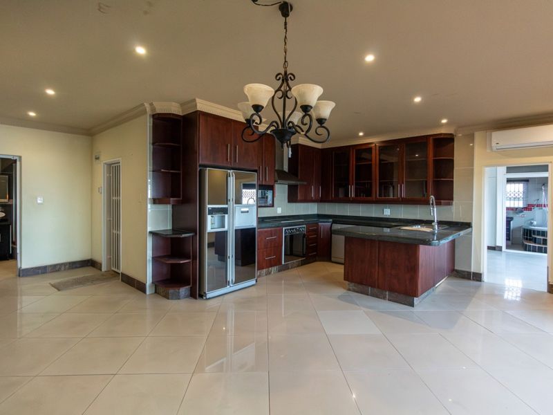Spacious kitchen featuring dark wood cabinetry, granite countertops, integrated appliances, and tiled flooring, with an open-plan layout and recessed lighting.