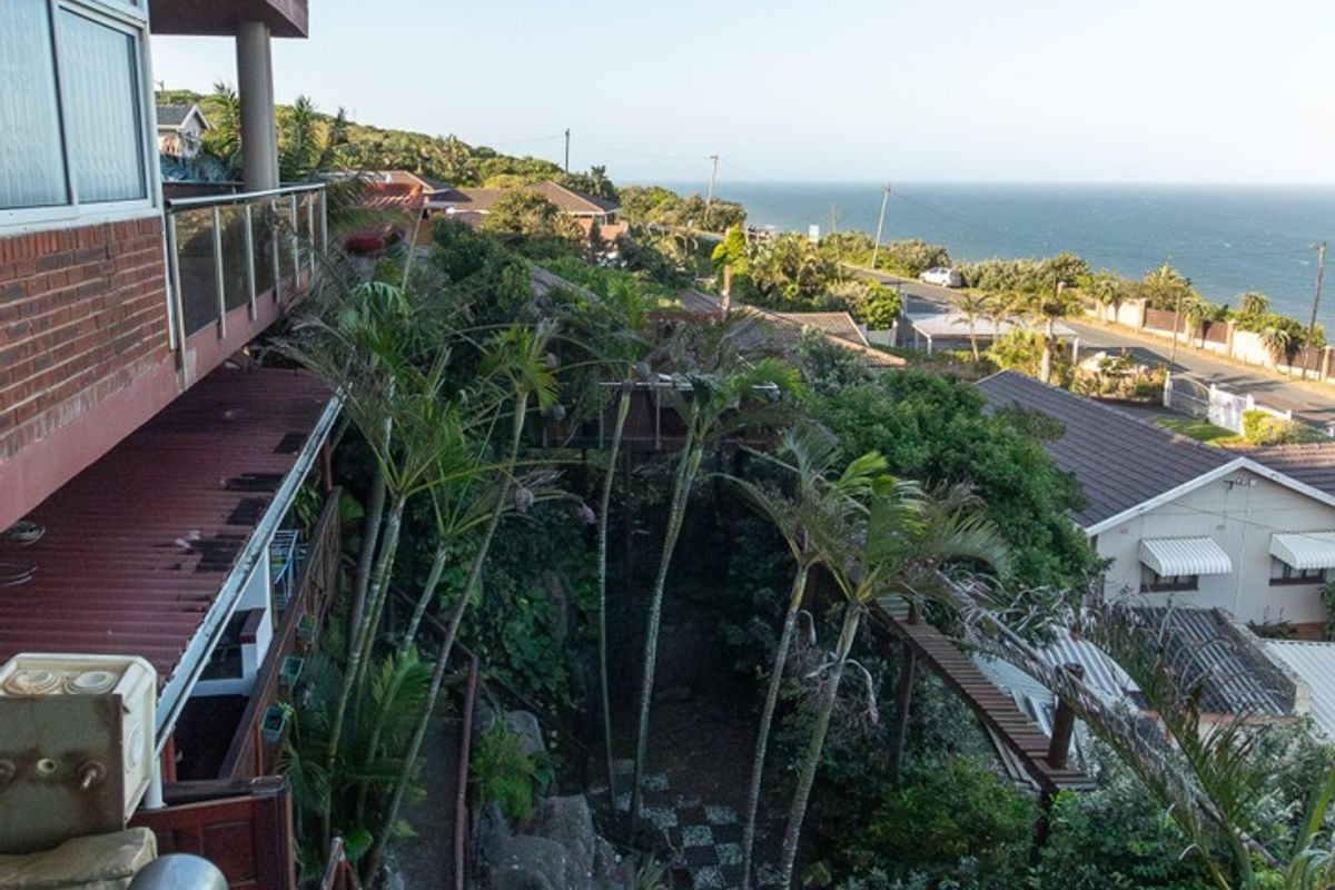 Elevated rear view of the property featuring a brick facade, glass balustrade, and a landscaped garden with stone retaining walls overlooking the coastline.