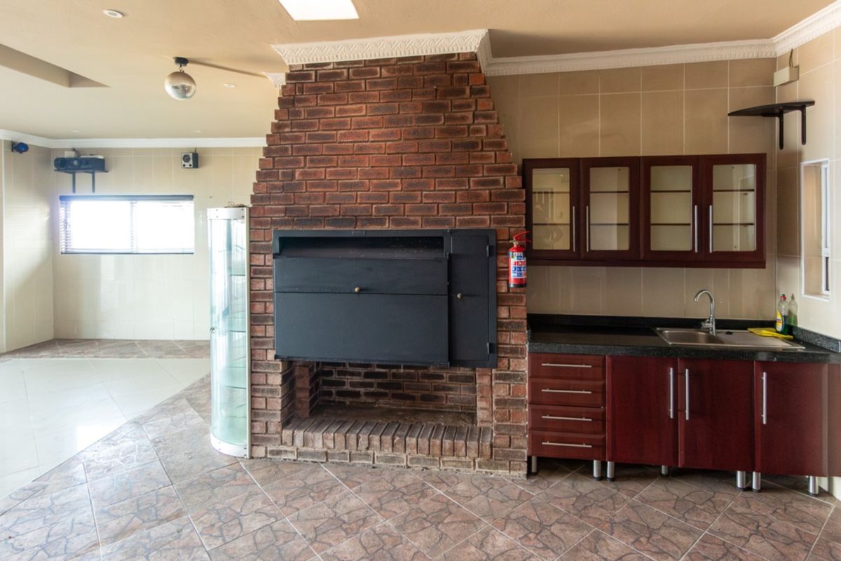 Spacious living area featuring a prominent built-in brick fireplace and braai, complemented by a functional kitchenette with dark wood cabinetry and granite countertops.