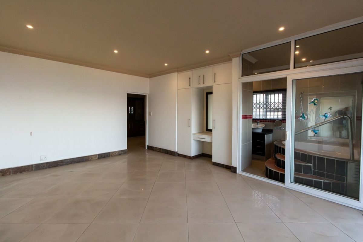Spacious bedroom featuring neutral tiled flooring, built-in cupboards with a vanity area, and direct access to an en-suite bathroom through a sliding glass door.