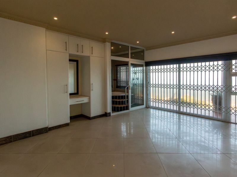 Spacious bedroom featuring tiled flooring, built-in cupboards with a vanity, recessed lighting, and a sliding door with security gate access.