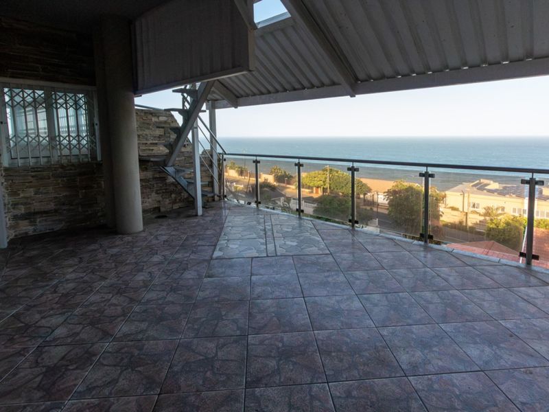 Spacious covered balcony featuring tiled flooring, a glass balustrade, and a spiral staircase, offering expansive ocean views.