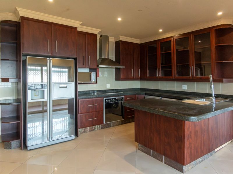 A well-appointed kitchen featuring dark wood cabinetry, granite countertops, a central island, and integrated stainless steel appliances with modern recessed lighting.