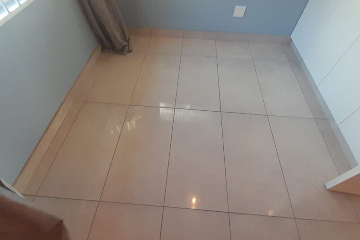 A clean, empty bedroom featuring neutral floor tiles, built-in cupboards, and a window with security bars.