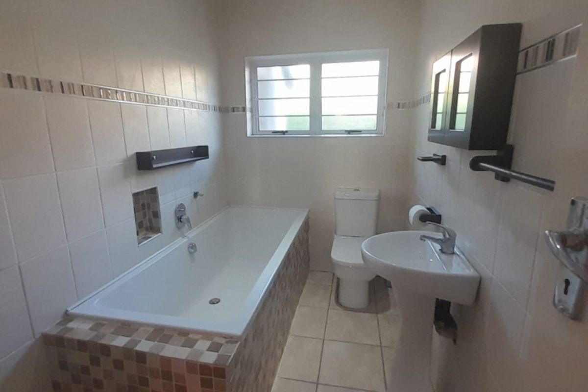 A functional bathroom featuring a built-in bathtub with mosaic tile surround, a pedestal basin, and a standard toilet.