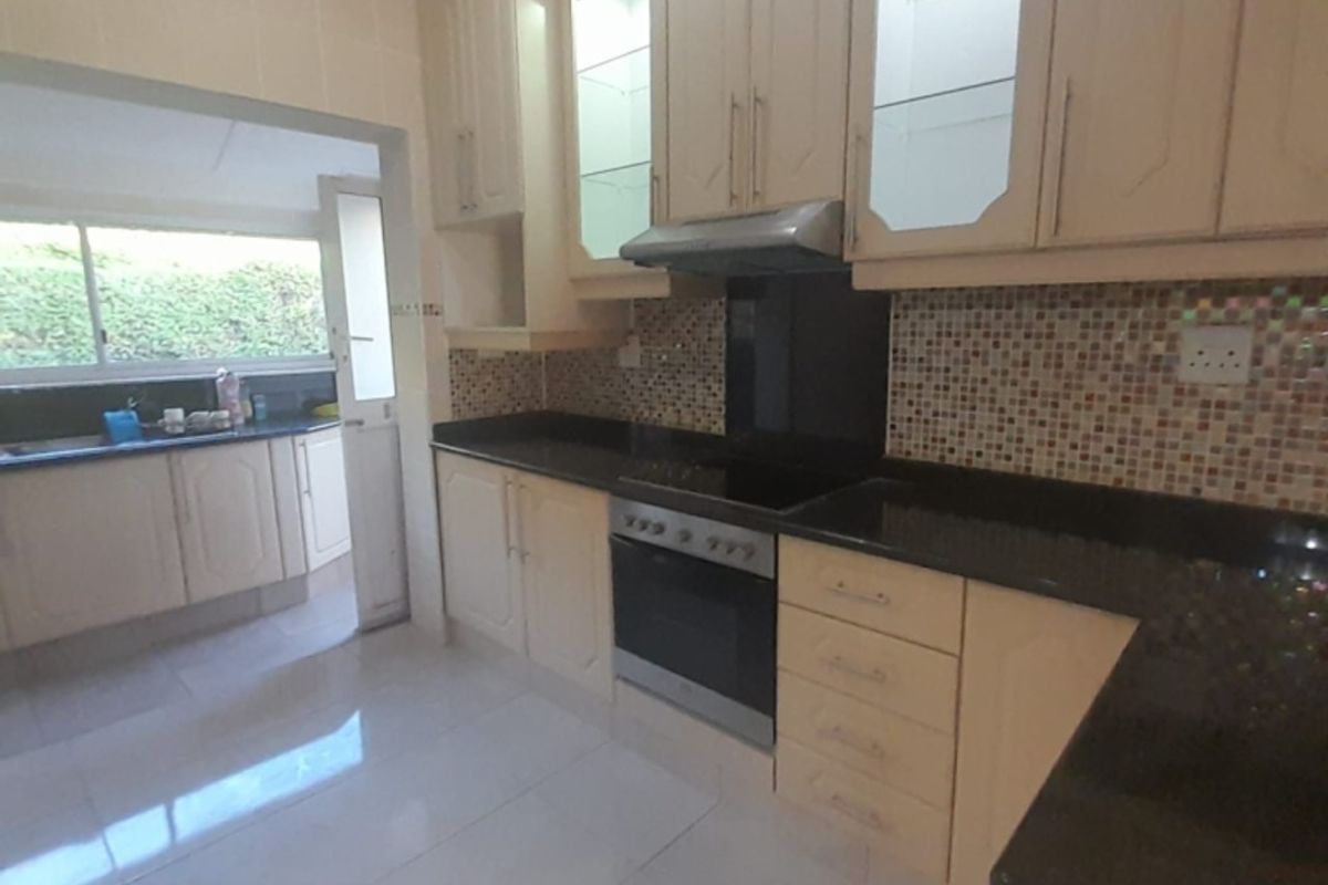 A functional kitchen featuring light-toned cabinetry, dark granite countertops, a built-in oven and hob, and a mosaic tile backsplash.