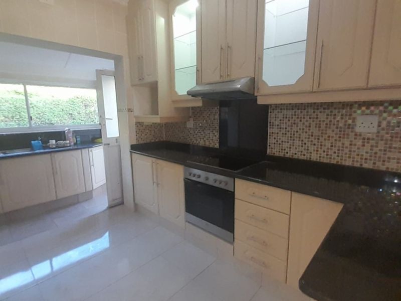 A functional kitchen featuring light-toned cabinetry, dark granite countertops, a built-in oven and hob, and a mosaic tile backsplash.