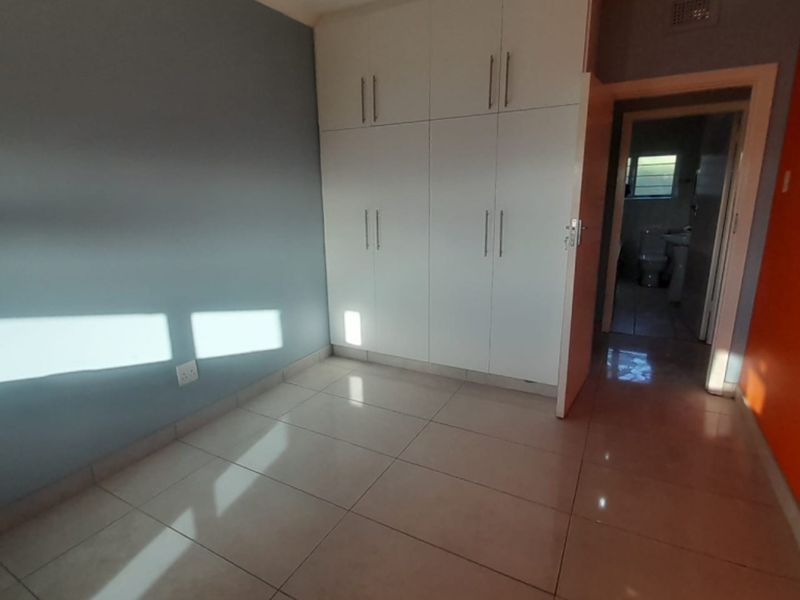 A bedroom featuring built-in cupboards, tiled flooring, and an adjacent doorway leading to a bathroom.
