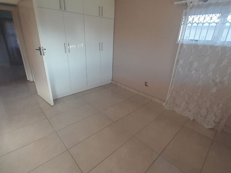 A bright, empty bedroom featuring neutral floor tiles and built-in white cabinetry with ample storage space.