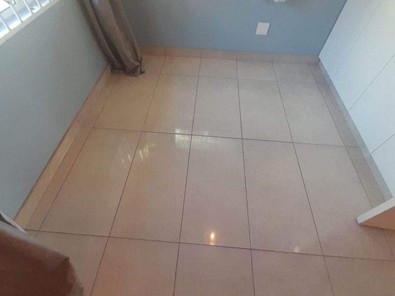 A clean, empty bedroom featuring neutral floor tiles, built-in cupboards, and a window with security bars.