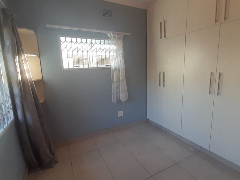 A bedroom featuring built-in white cabinetry, tiled flooring, and security bars on the windows.