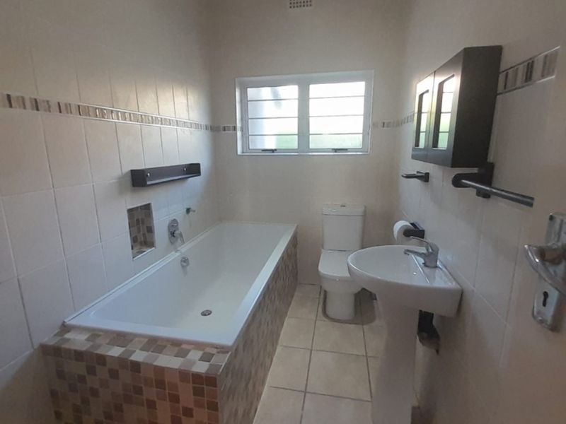 A functional bathroom featuring a built-in bathtub with mosaic tile surround, a pedestal basin, and a standard toilet.