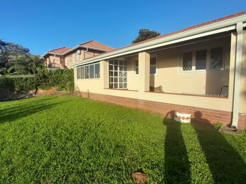 A view of the rear exterior of the house, featuring a covered patio area, brick base, and a well-maintained lawn.