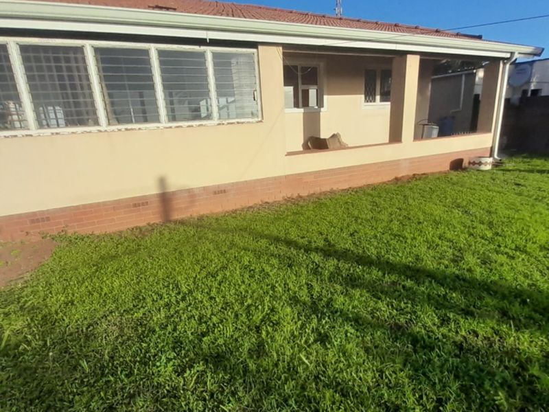 Rear view of the house featuring a covered patio area, brick base, and a spacious lawn.