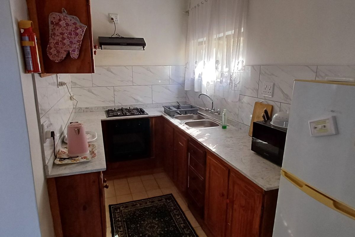 A functional kitchen featuring wooden cabinetry, stone-look countertops, a gas hob, built-in oven, and a tiled backsplash.